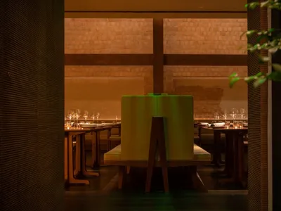 Modern restaurant dining room with green chairs and wooden tables, illuminated by soft lighting and surrounded by greenery.