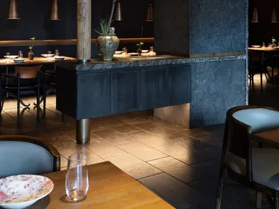 A modern, industrial restaurant interior featuring stone columns and metal framed windows.