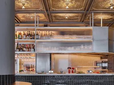 Modern restaurant bar counter featuring a terrazzo floor, glass shelves, and metallic bar stools.
