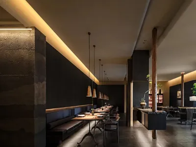 Modern restaurant interior with concrete walls, wooden tables, and metal pendant lights.
