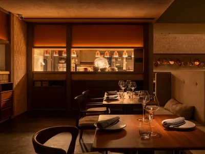 Modern restaurant interior with a counter made of brass and wood, against a brick wall