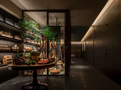 Modern restaurant entryway featuring wooden flooring and cabinets with glass doors displaying food items and plants.