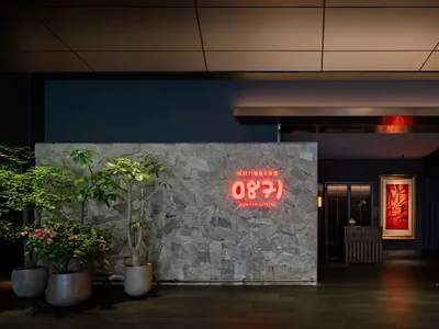 A modern restaurant interior with concrete walls, plants, and a neon sign.