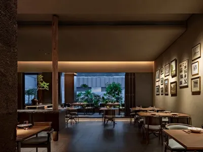 A modern restaurant interior featuring wooden tables, stone details, and green plants.
