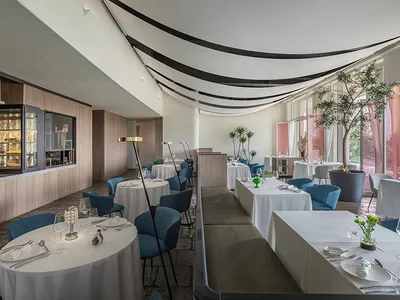 Modern, brightly-lit restaurant interior with white tables and blue chairs.