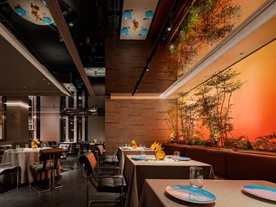 A modern restaurant interior with sleek concrete flooring, metal accents, and glass walls.