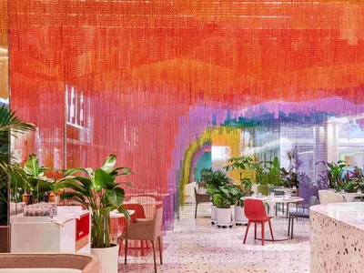 A contemporary restaurant interior featuring orange drapery and various plants and furniture.