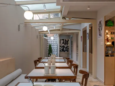 A minimalist restaurant with white walls, wooden tables, and modern lighting fixtures.