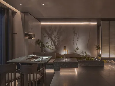 A minimalist restaurant interior featuring stone tables and wooden sofas on a polished concrete floor, with a small indoor ga