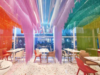 A modern restaurant with colorful terrazzo flooring and hanging rainbow curtains.