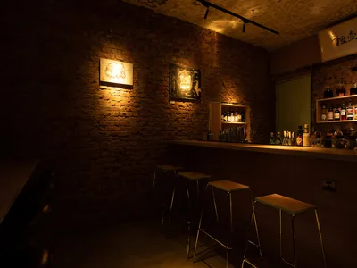 A dimly lit restaurant bar with brick walls, industrial lighting, and a wooden counter.