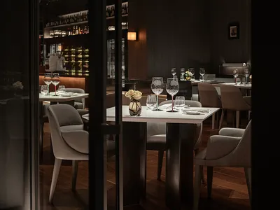 Modern restaurant interior with glass walls and tables.