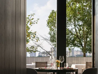 Modern restaurant interior view showcasing contemporary dining setting with large windows overlooking cityscape and greenery.