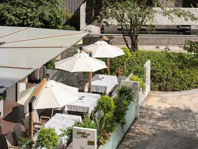 Outdoor seating area with white tables, umbrellas, and potted plants in a contemporary design setting.