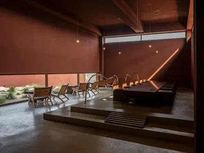 Modern restaurant interior with concrete floors, minimalist furniture, and a large window allowing natural light to enter.