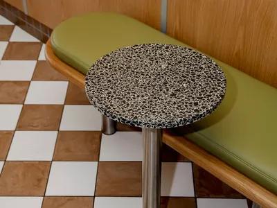 A modern restaurant interior with a round, speckled black countertop on a checkered tile floor.