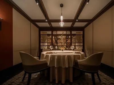 A modern restaurant interior with a round table set for a meal, featuring wood chairs and a circular light fixture.