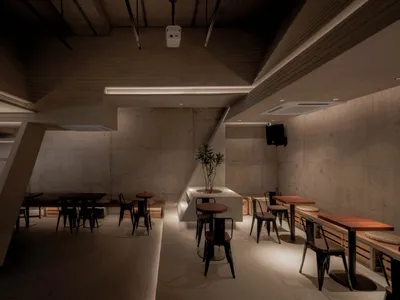 A modern, industrial-themed restaurant with concrete walls, wooden tables, and metal chairs.
