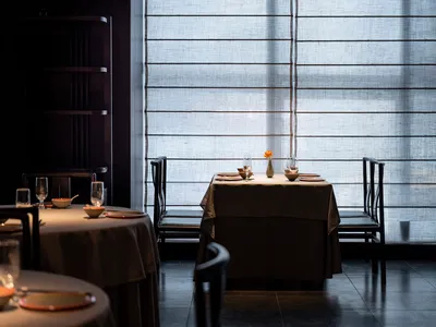 A minimalist restaurant interior featuring fabric curtains and wooden flooring.