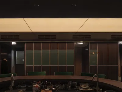 A dimly lit industrial restaurant bar counter with wooden panels and green seating.