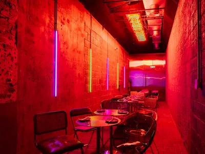 A brightly lit industrial restaurant interior with concrete walls adorned with neon lights.