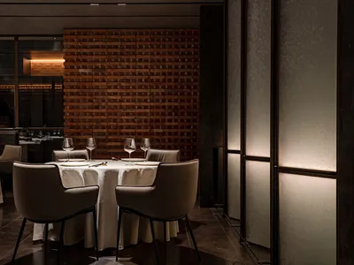 昏暗照明的餐廳，磚牆背景，圓桌擺設四人餐具，以及流線型現代餐椅。