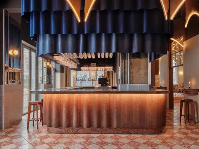Modern bar interior with wooden counter and stools, featuring hanging glasses and illuminated lighting.