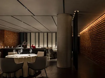 Modern restaurant with brick and concrete interior, featuring round tables, chairs, and minimalist decor.