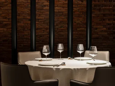 A modern restaurant setting with a brick wall and leather chairs.