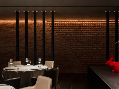 A modern restaurant interior with a brick wall backdrop, showcasing a round dining table set for four with white tablecloth a