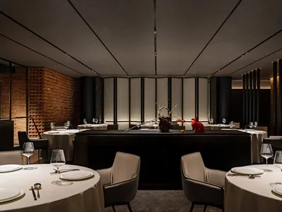 A modern restaurant interior with brick and concrete materials, featuring tables set for dining.