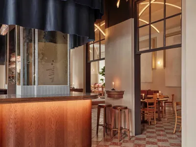 Interior of a modern restaurant with wooden bar counter, terrazzo flooring, and glass windows.