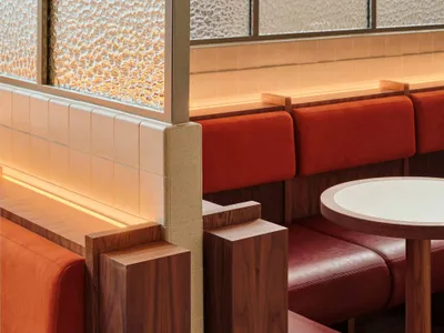 Modern restaurant interior with leather seating, wood furnishings, and concrete walls.