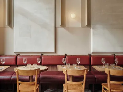 Modern restaurant interior with wooden chairs, leather benches, and red cushions.