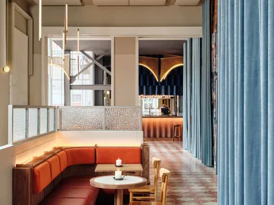 A modern cafe interior featuring red leather banquettes and white marble tiles.