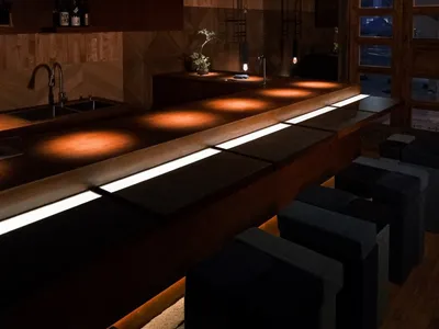 A modern restaurant bar with wooden interiors, neon lights, and comfortable seating