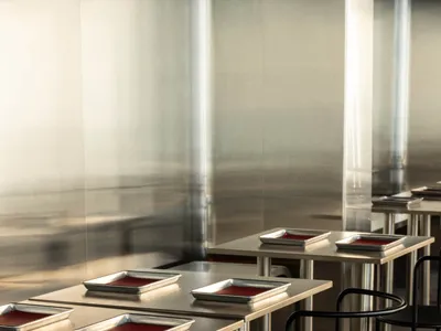 A sleek, modern restaurant interior featuring metal and black tables and chairs with red dishes.