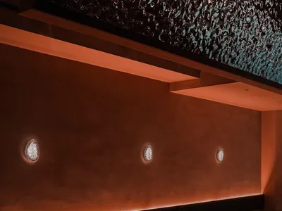 Modern restaurant interior with metal clad panel, orange chairs, and round tables.