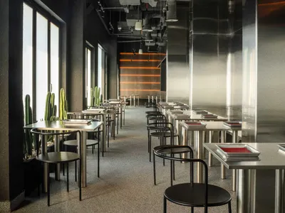 An empty, industrial-style restaurant with long tables, black chairs, and glass partitions.