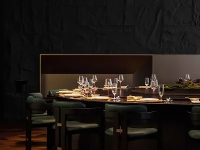 A modern restaurant interior featuring a circular dining table with black marble material and green chairs.