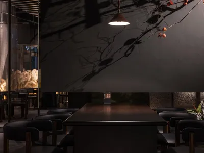 A modern restaurant interior with black walls, dark wood furniture, and a black stone counter, featuring a patterned glass pa