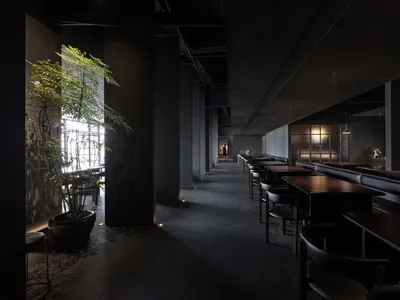 Modern restaurant interior with concrete walls, glass panels, and metal furniture.