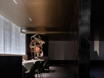 A minimalist restaurant interior with black, white, and metallic elements, featuring a modern hanging sculpture and a waterfa