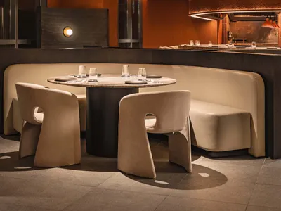 A minimalist restaurant interior with circular leather seating, a round table, and a large, illuminated chandelier hanging fr