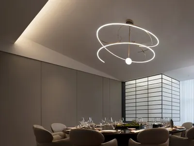 A modern restaurant dining room with a metallic chandelier and dark wooden flooring.