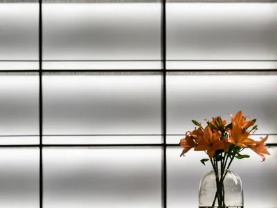 Modern restaurant table setting with white tablecloth, red-bottomed wine glasses, and orange lilies in a vase.