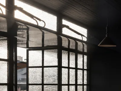 Interior view of an industrial-style restaurant with glass walls, wooden tables, and metal accents.