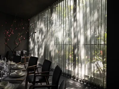 A modern restaurant dining area with sheer curtains, glass walls, and minimalist black chairs.