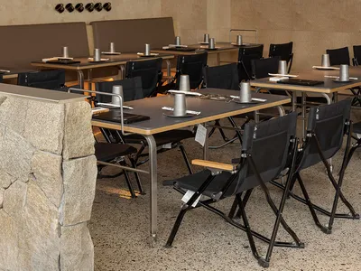 A modern restaurant interior with wooden tables and chairs, featuring a stone pillar and a wine rack on the wall.
