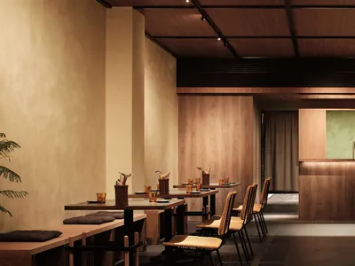 Modern restaurant interior with wooden tables, chairs, and walls, featuring minimalist design.